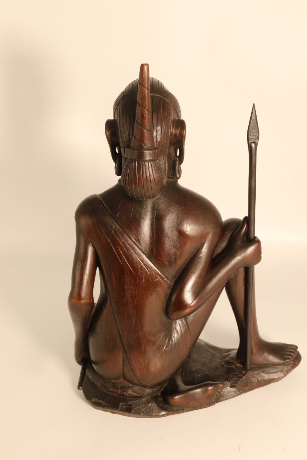A dark hardwood hand-carved sculpture of a kneeling Maasai warrior holding a spear and club on an integrated wooden base. View V