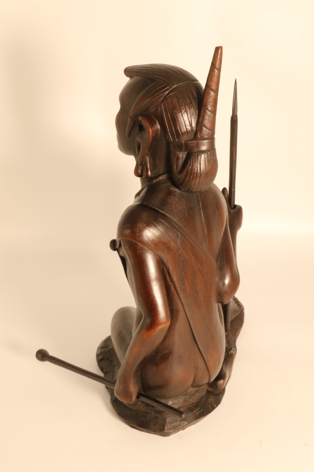 A dark hardwood hand-carved sculpture of a kneeling Maasai warrior holding a spear and club on an integrated wooden base. View VI