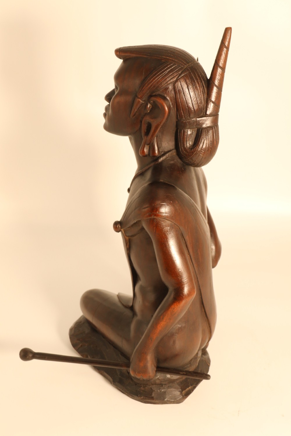 A dark hardwood hand-carved sculpture of a kneeling Maasai warrior holding a spear and club on an integrated wooden base. View VII