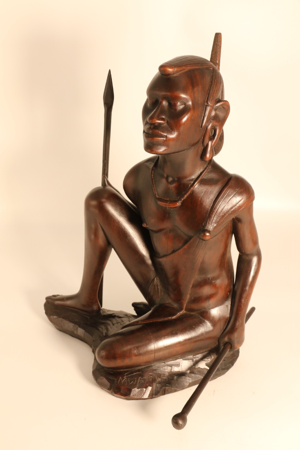 A dark hardwood hand-carved sculpture of a kneeling Maasai warrior holding a spear and club on an integrated wooden base. View IX