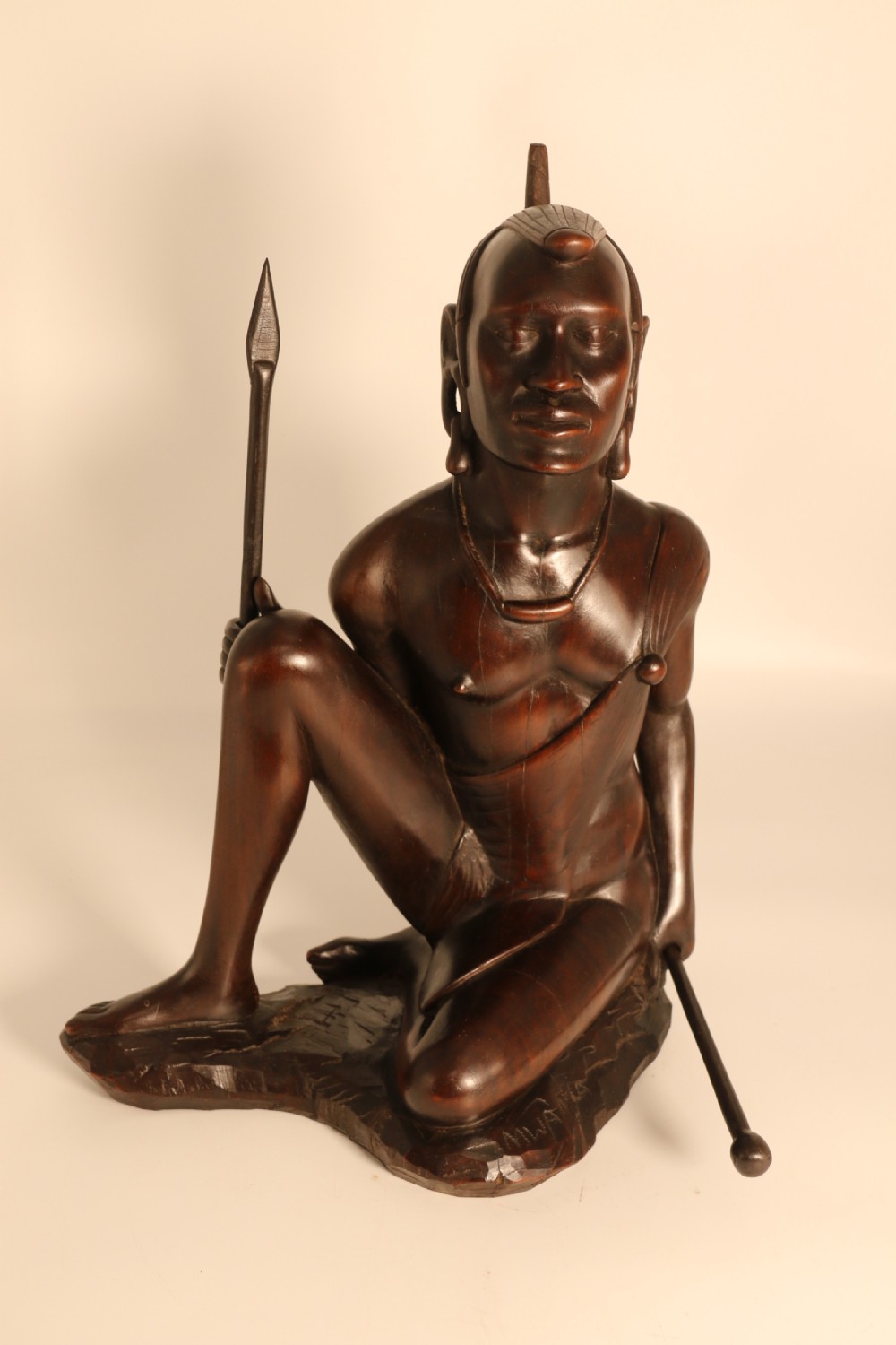 A dark hardwood hand-carved sculpture of a kneeling Maasai warrior holding a spear and club on an integrated wooden base. View XI