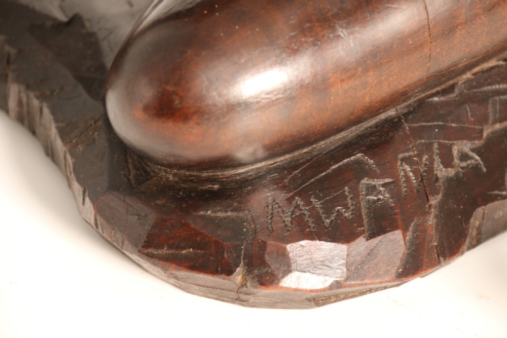 A dark hardwood hand-carved sculpture of a kneeling Maasai warrior holding a spear and club on an integrated wooden base. View XII
