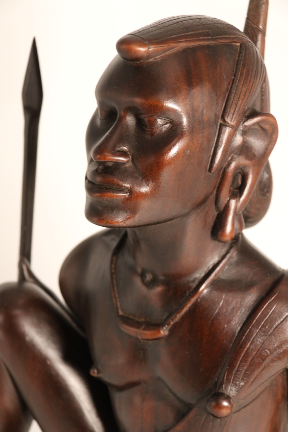 A dark hardwood hand-carved sculpture of a kneeling Maasai warrior holding a spear and club on an integrated wooden base. View XIV