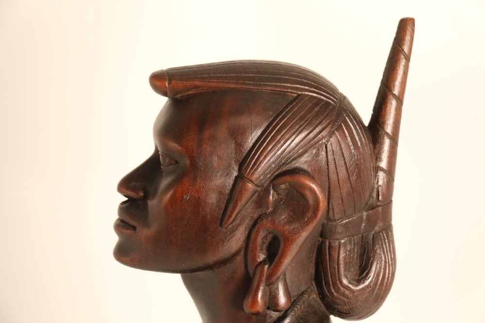 A dark hardwood hand-carved sculpture of a kneeling Maasai warrior holding a spear and club on an integrated wooden base. View XV