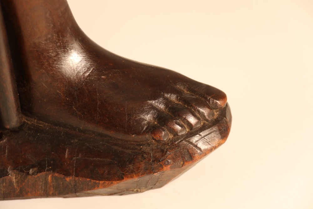 A dark hardwood hand-carved sculpture of a kneeling Maasai warrior holding a spear and club on an integrated wooden base. View XVI