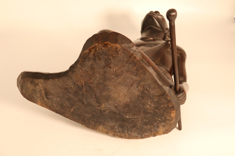 A dark hardwood hand-carved sculpture of a kneeling Maasai warrior holding a spear and club on an integrated wooden base. View XIX