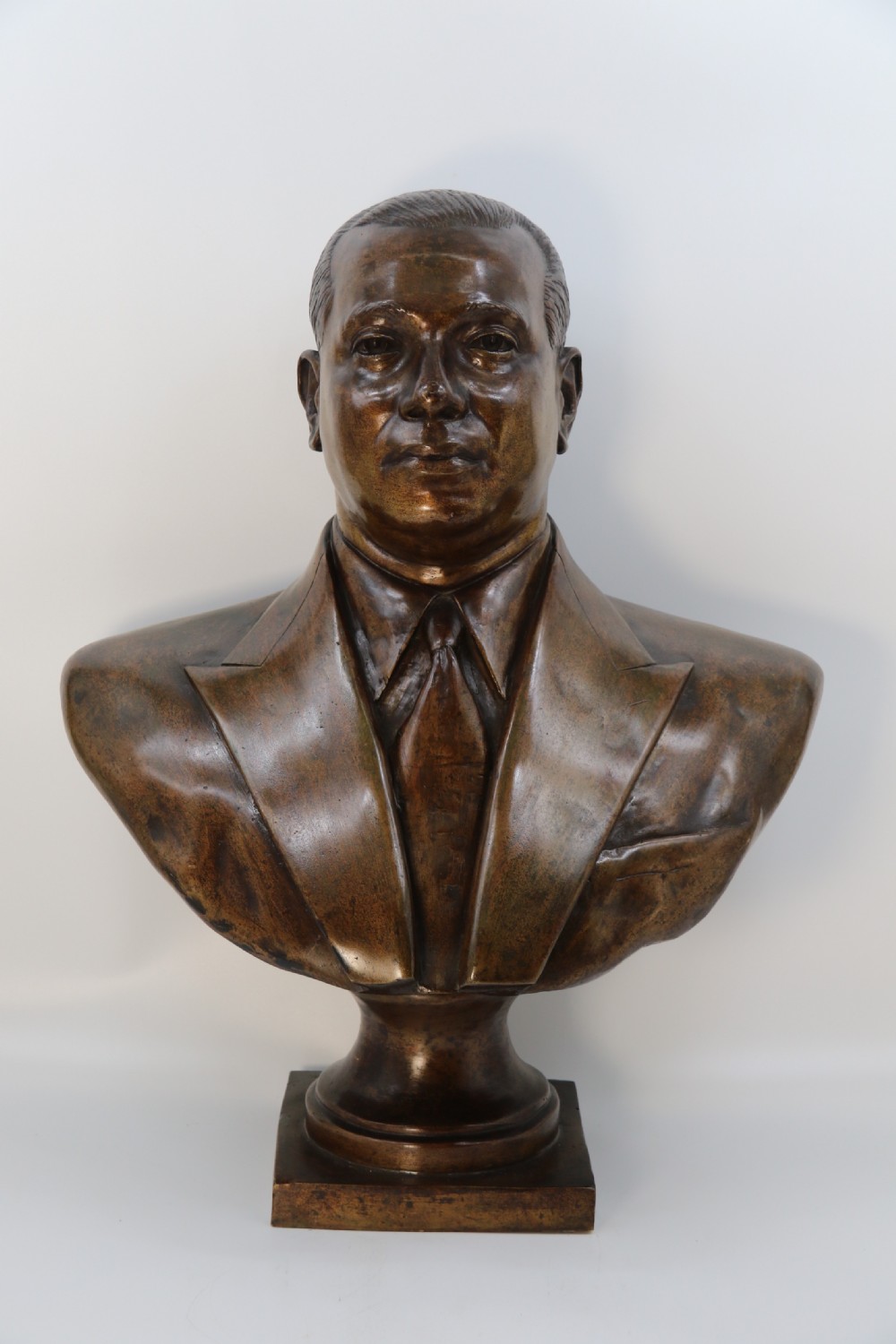 A cast bronze portrait bust depicting a gentleman in a suit jacket and tie, resting on a pedestal base with a square plinth. View III