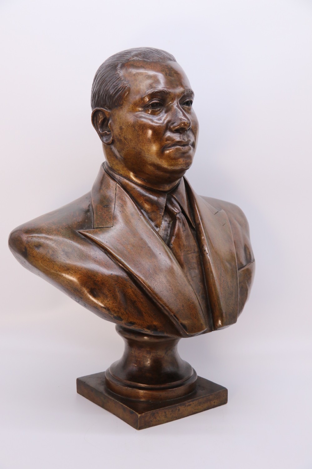 A cast bronze portrait bust depicting a gentleman in a suit jacket and tie, resting on a pedestal base with a square plinth. View IV