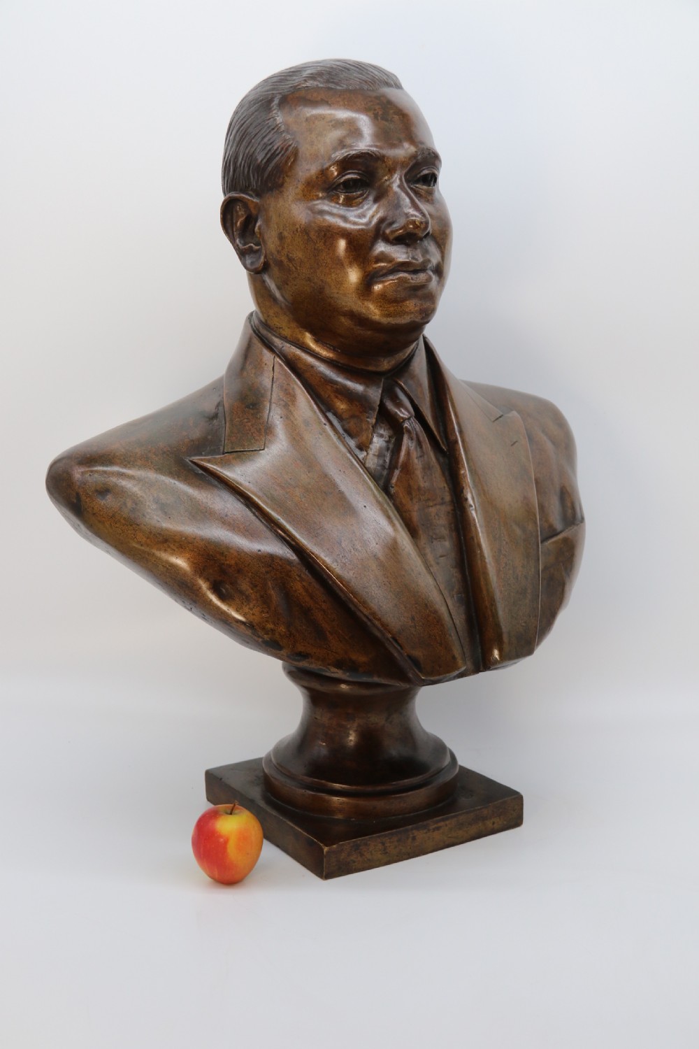 A cast bronze portrait bust depicting a gentleman in a suit jacket and tie, resting on a pedestal base with a square plinth. View V