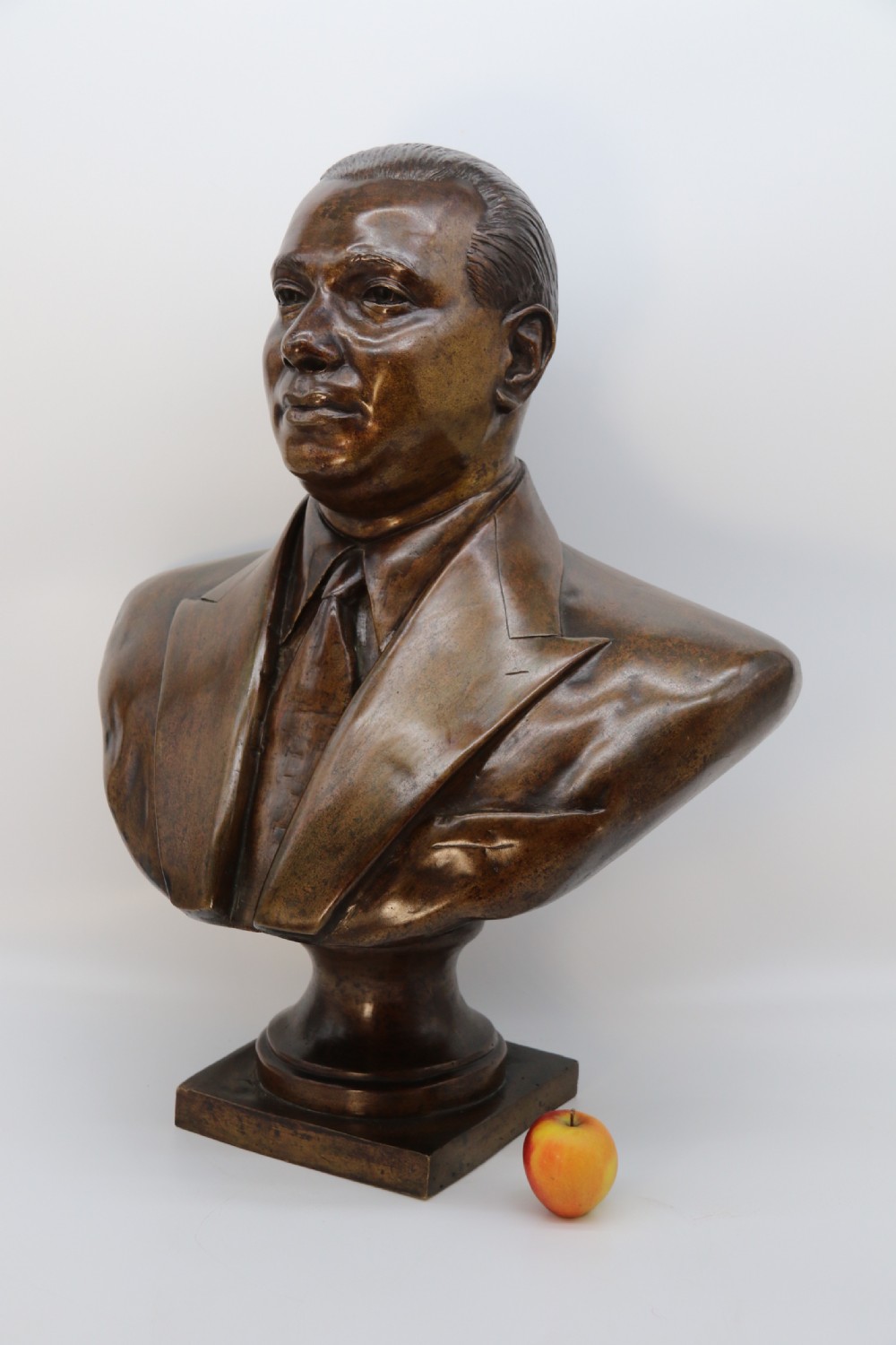 A cast bronze portrait bust depicting a gentleman in a suit jacket and tie, resting on a pedestal base with a square plinth. View VI