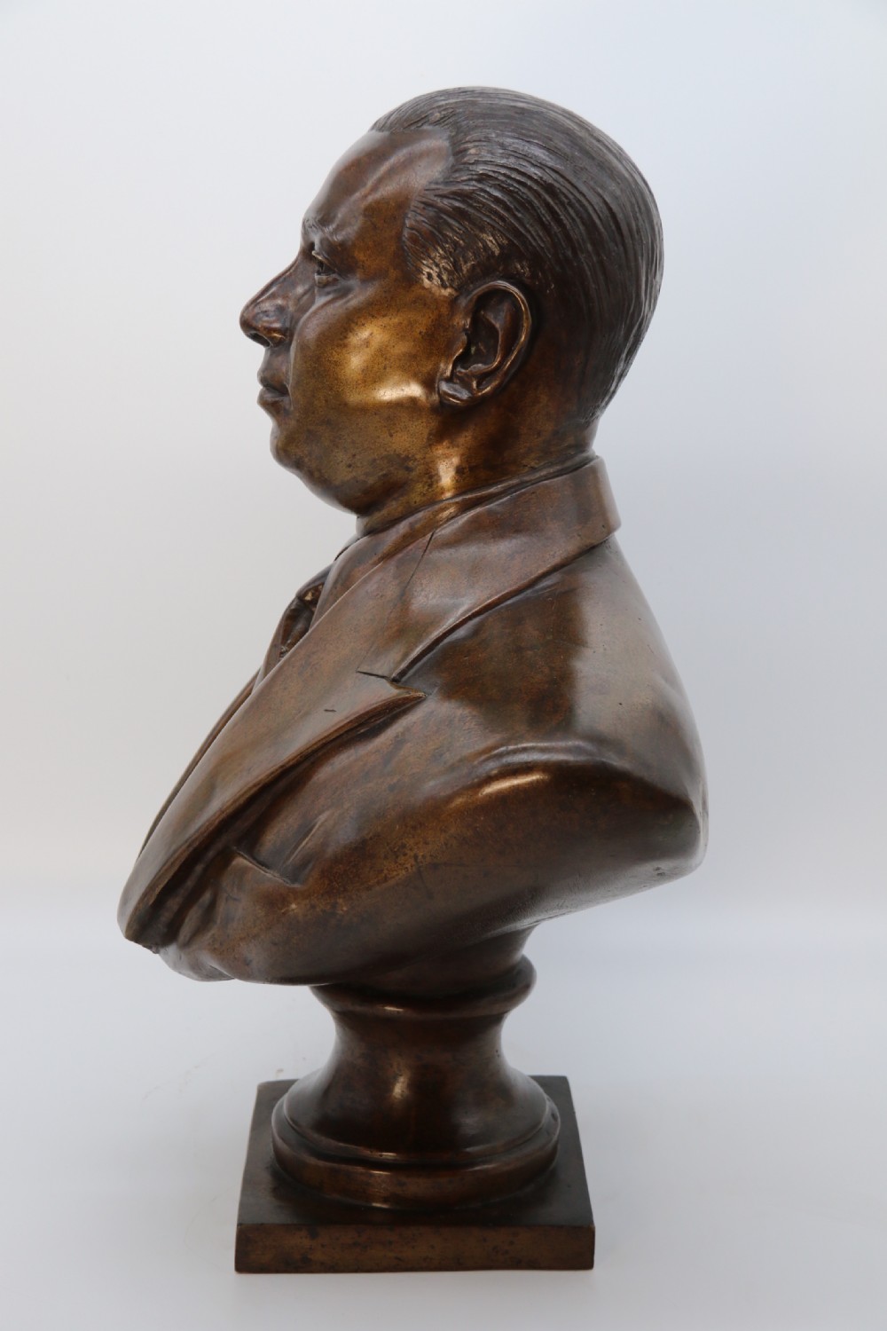 A cast bronze portrait bust depicting a gentleman in a suit jacket and tie, resting on a pedestal base with a square plinth. View VIII