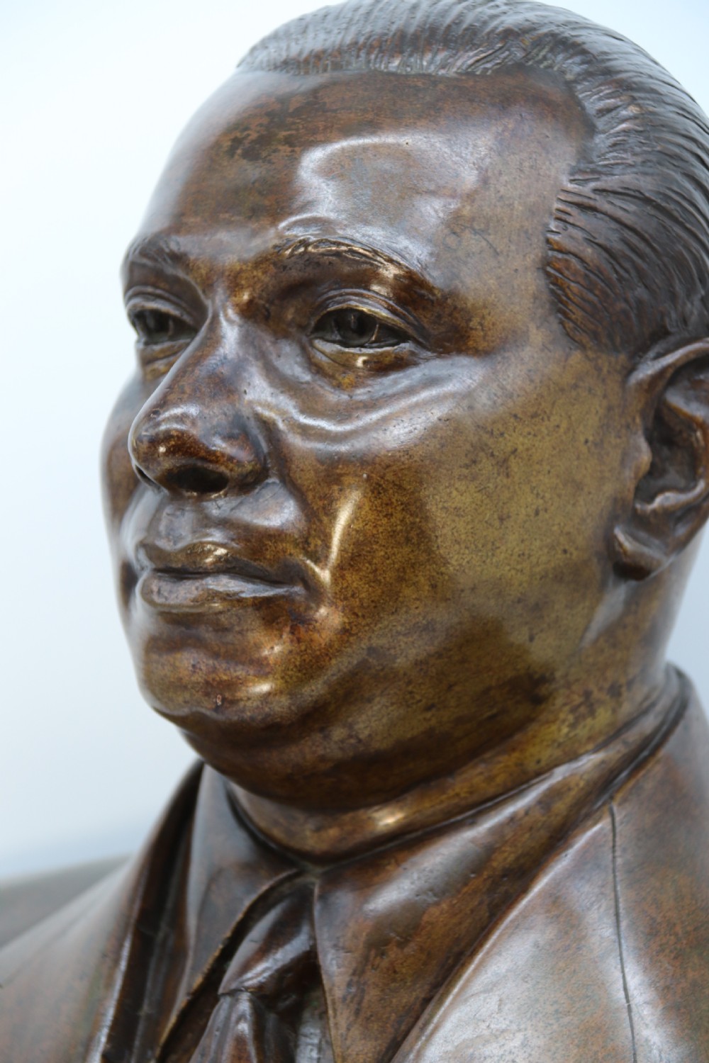 A cast bronze portrait bust depicting a gentleman in a suit jacket and tie, resting on a pedestal base with a square plinth. View XI