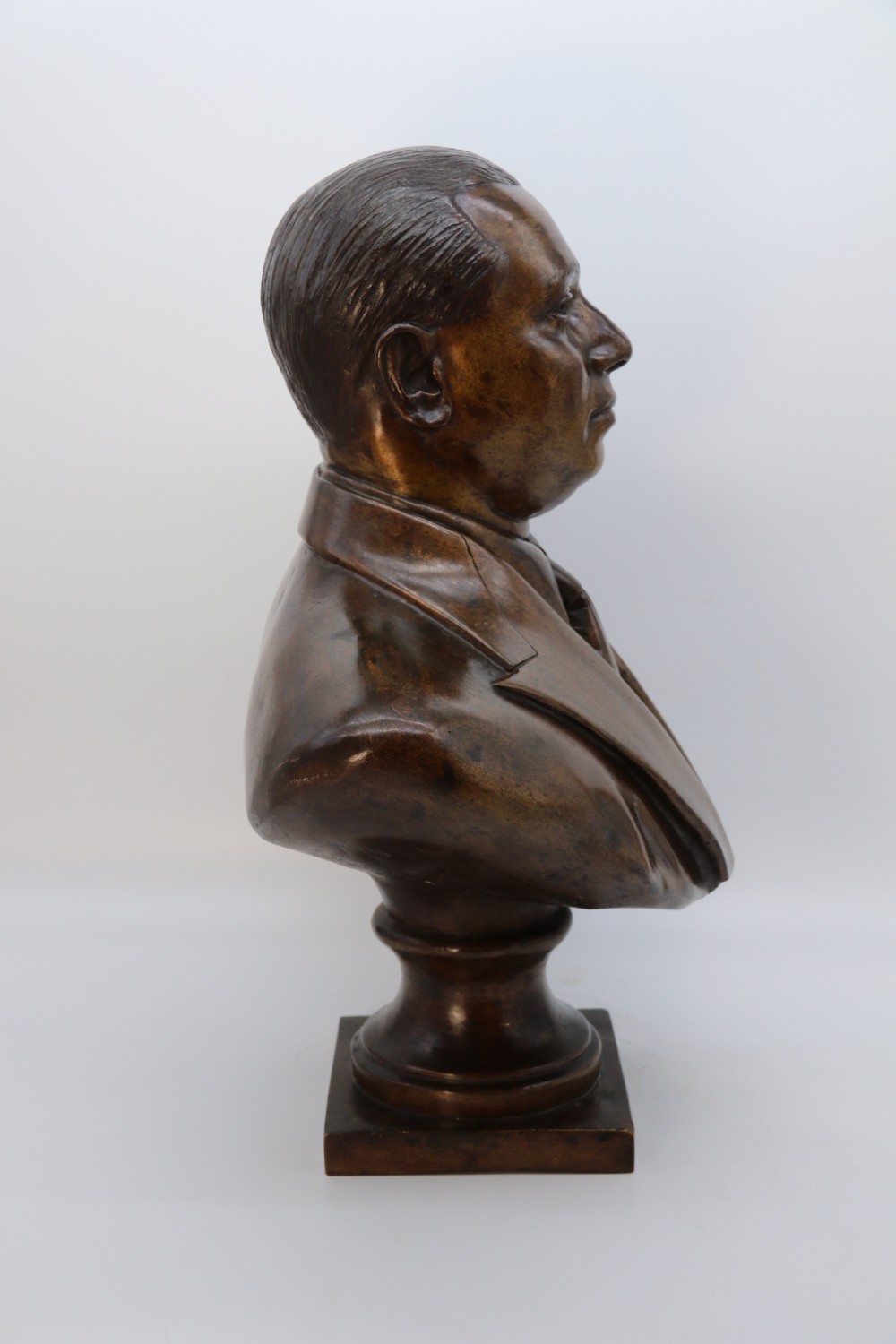 A cast bronze portrait bust depicting a gentleman in a suit jacket and tie, resting on a pedestal base with a square plinth. View XIII