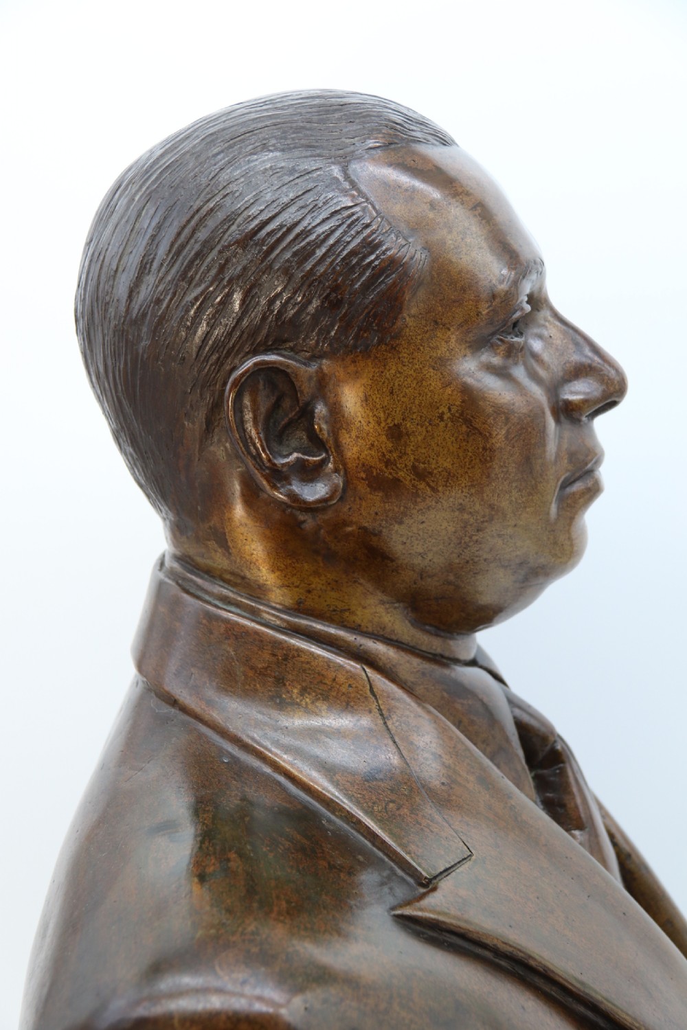A cast bronze portrait bust depicting a gentleman in a suit jacket and tie, resting on a pedestal base with a square plinth. View XIV