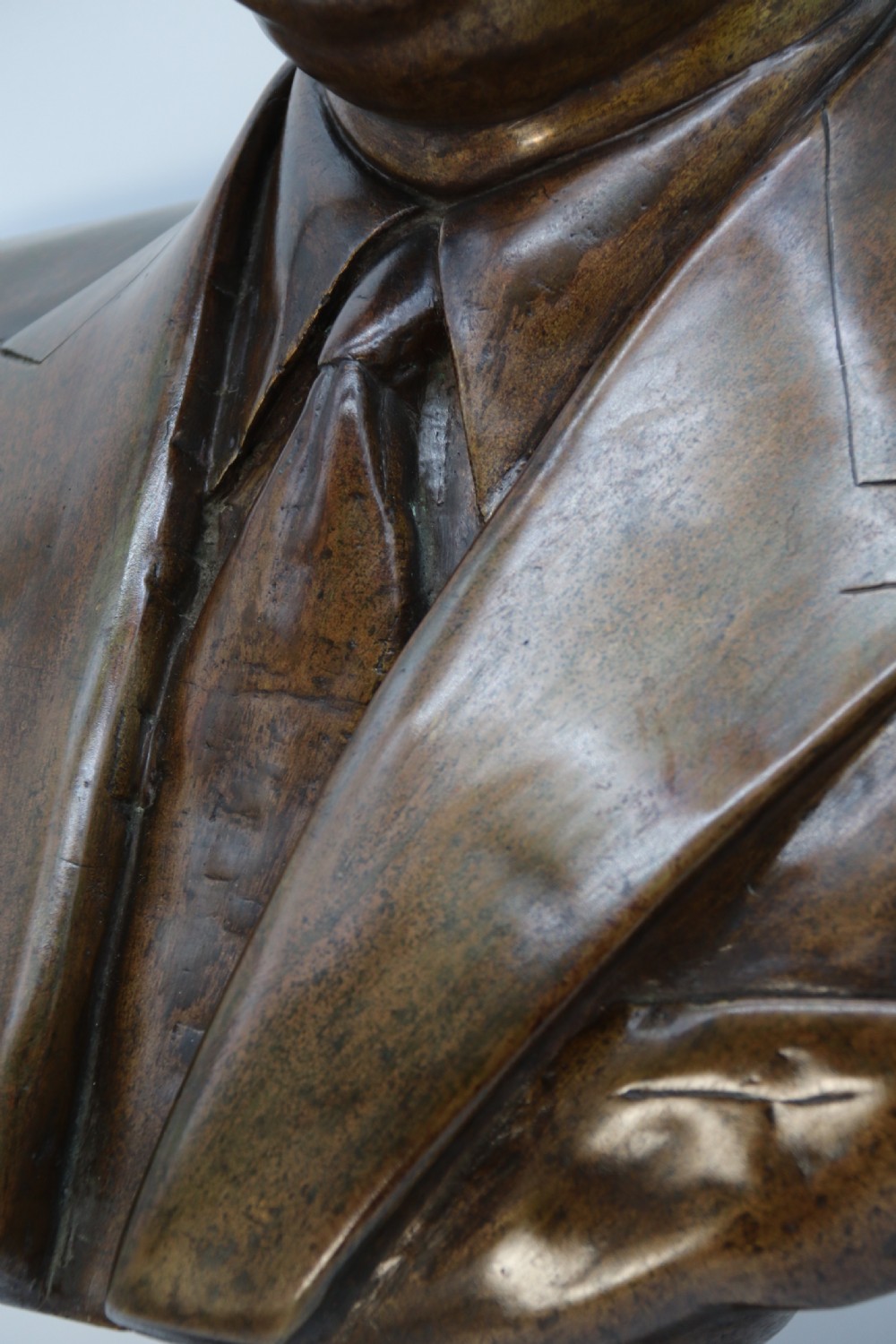 A cast bronze portrait bust depicting a gentleman in a suit jacket and tie, resting on a pedestal base with a square plinth. View XXI