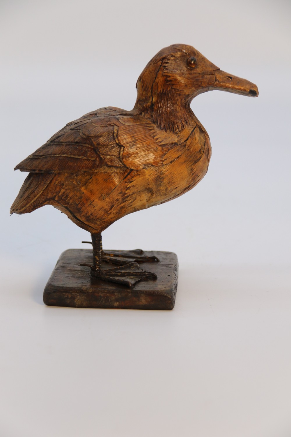 A small folk art duckling sculpture crafted from papier mache and textured straw, mounted on a square wooden base. View V