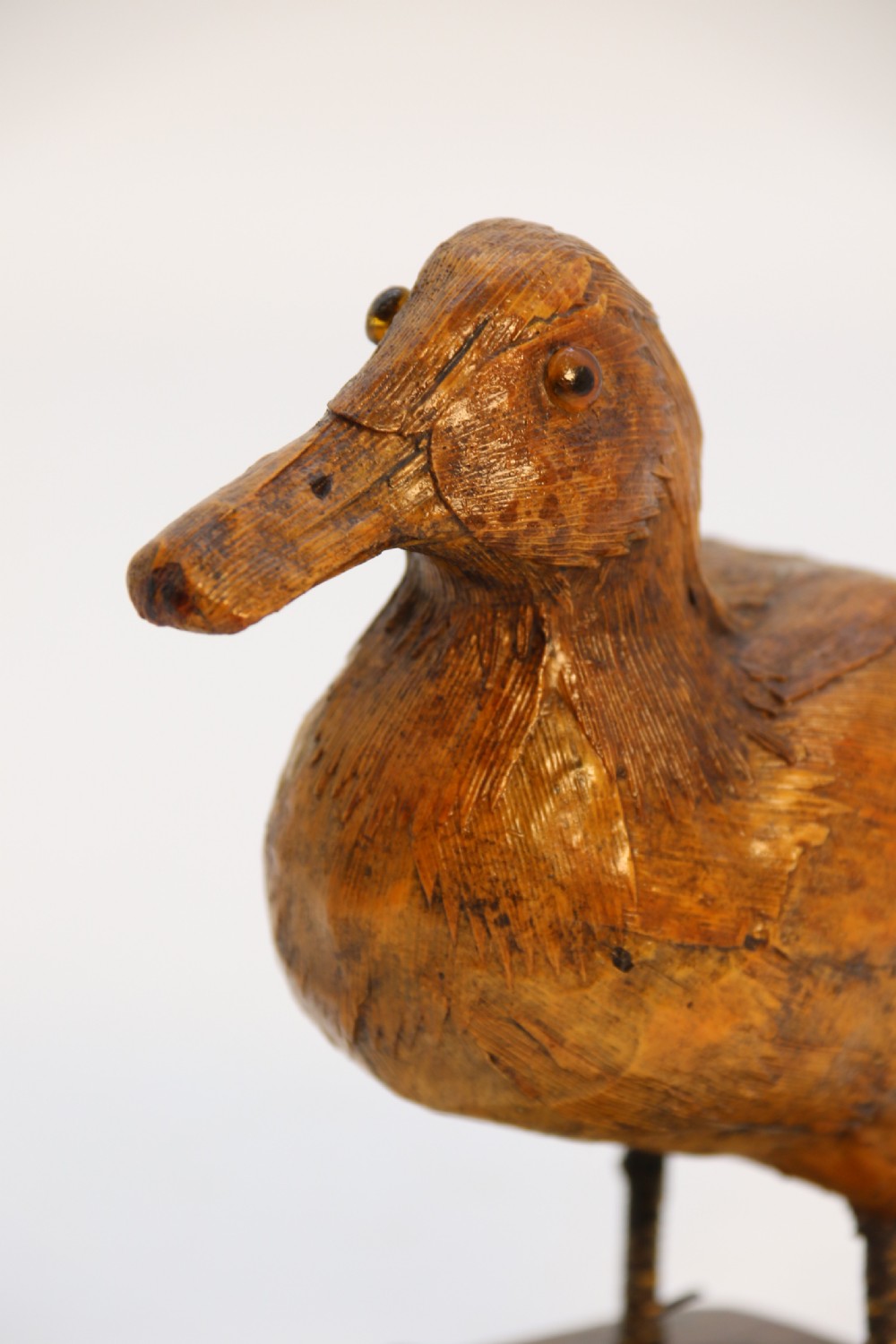 A small folk art duckling sculpture crafted from papier mache and textured straw, mounted on a square wooden base. View X