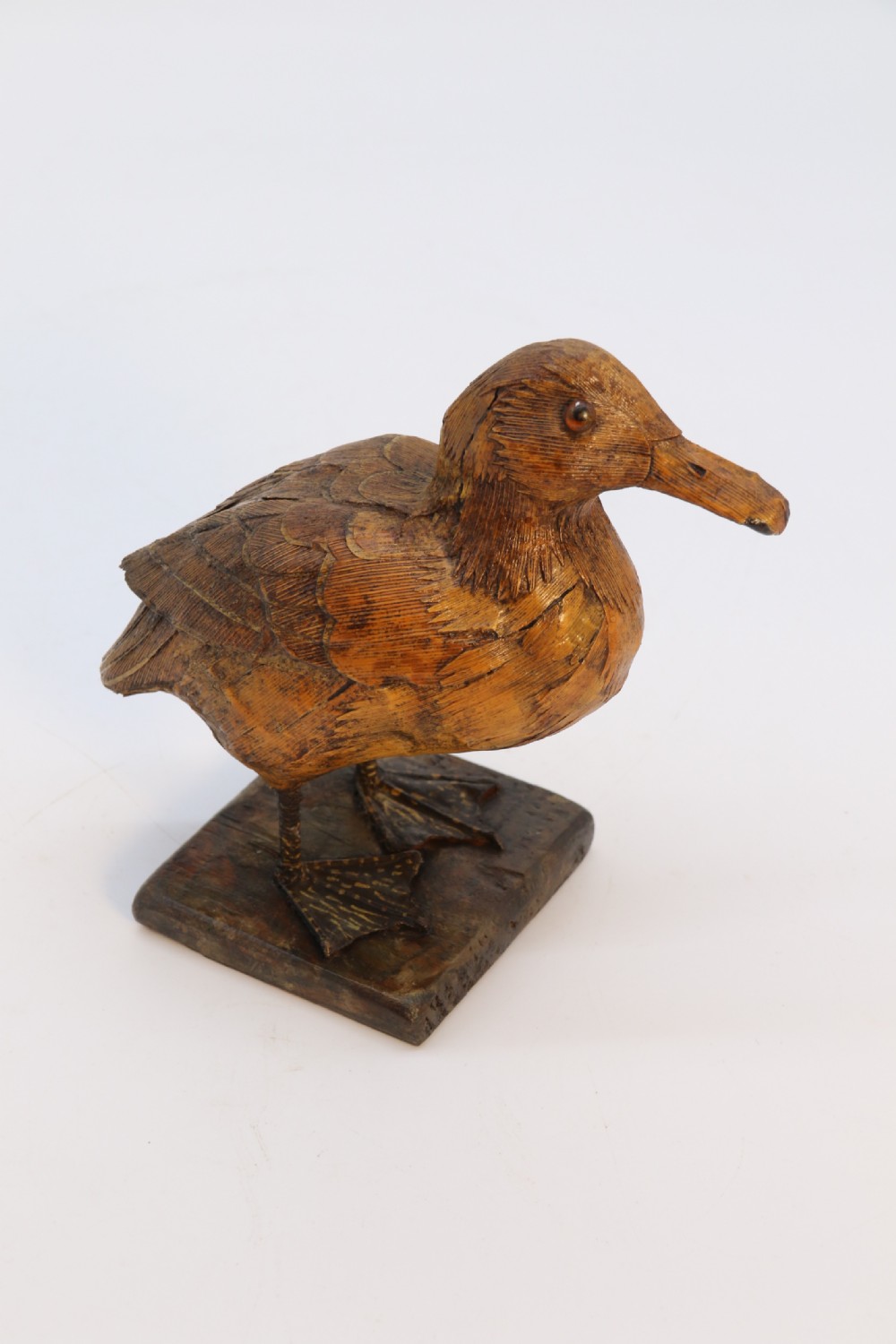A small folk art duckling sculpture crafted from papier mache and textured straw, mounted on a square wooden base. View XV