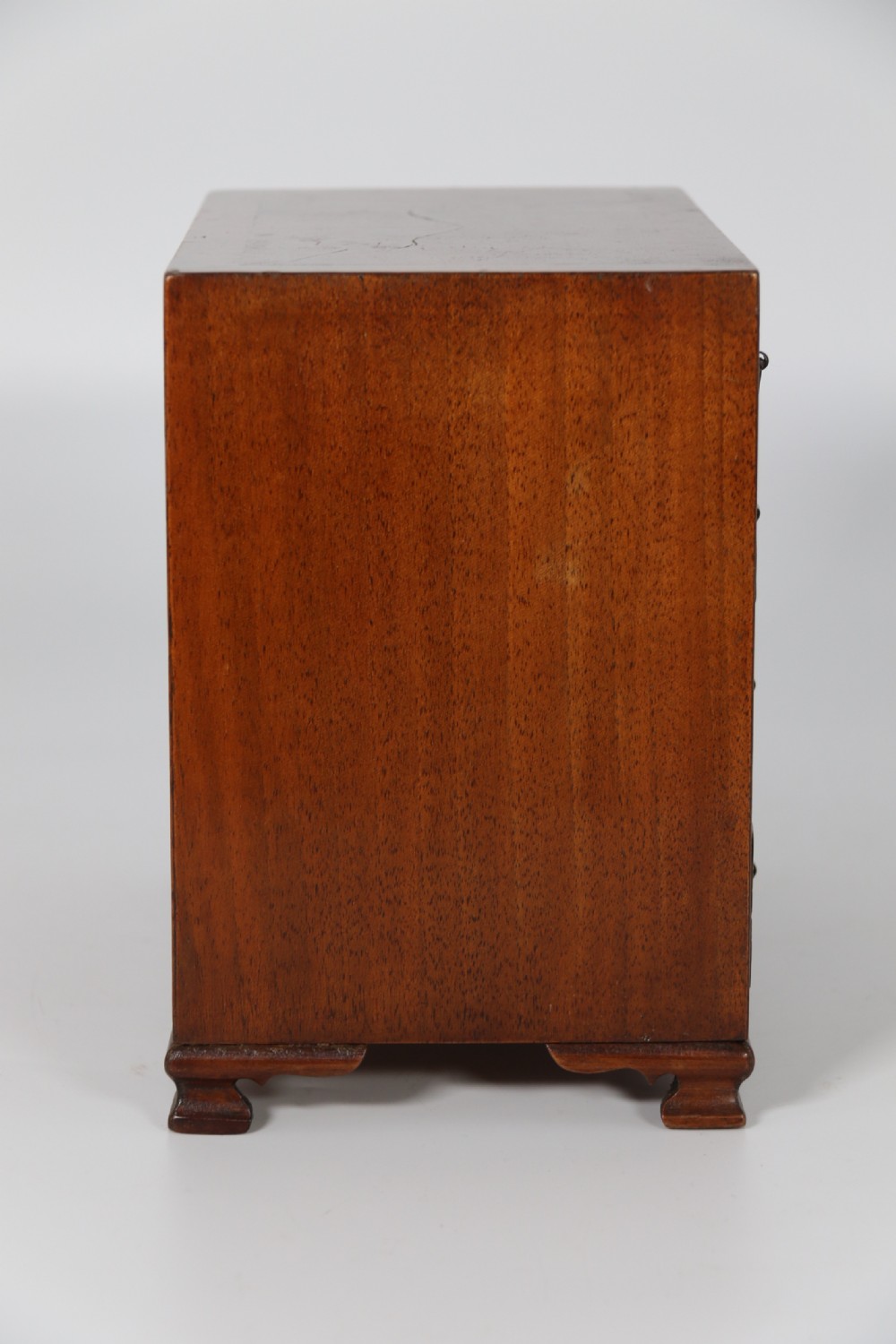 A miniature George II style chest of drawers crafted from figured walnut with brass drop handles, standing 20cm high beside a red apple for scale. View VI