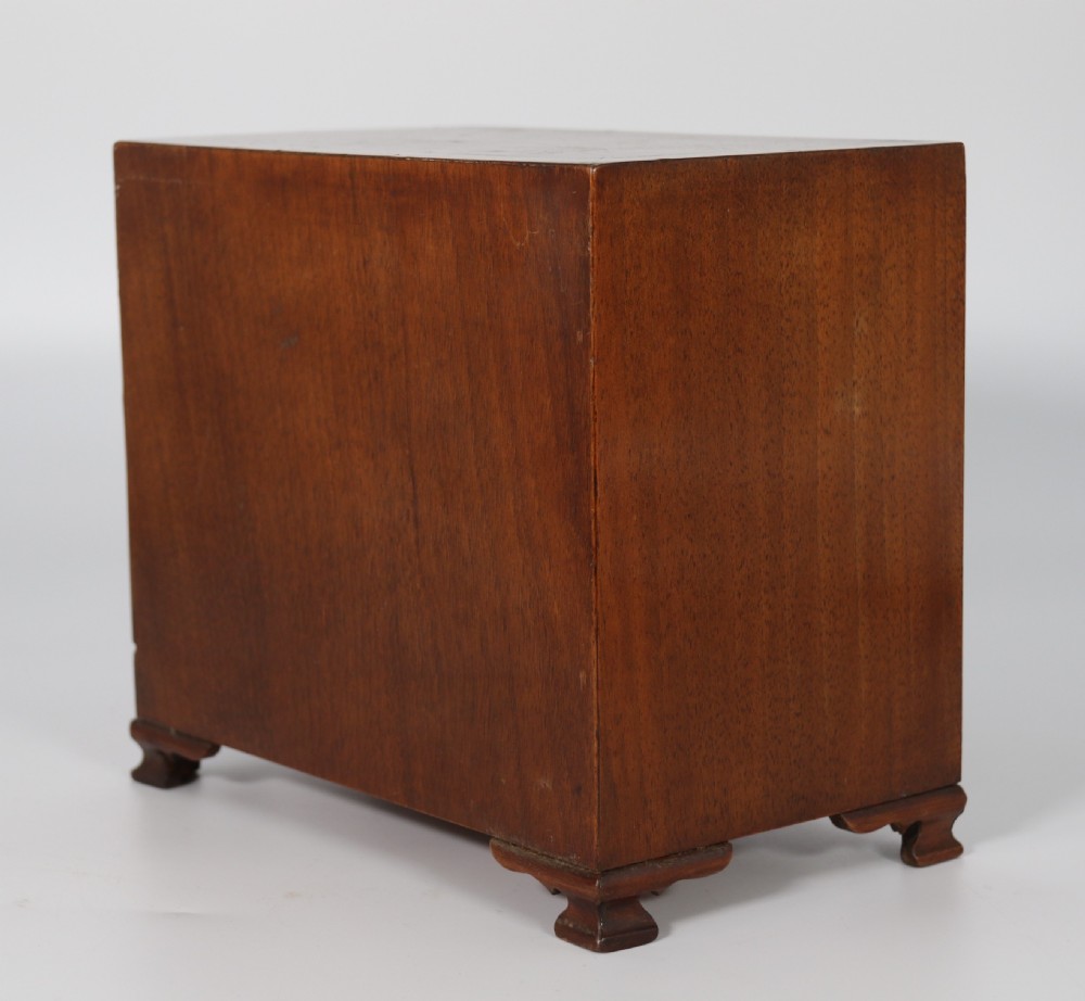 A miniature George II style chest of drawers crafted from figured walnut with brass drop handles, standing 20cm high beside a red apple for scale. View XVIII