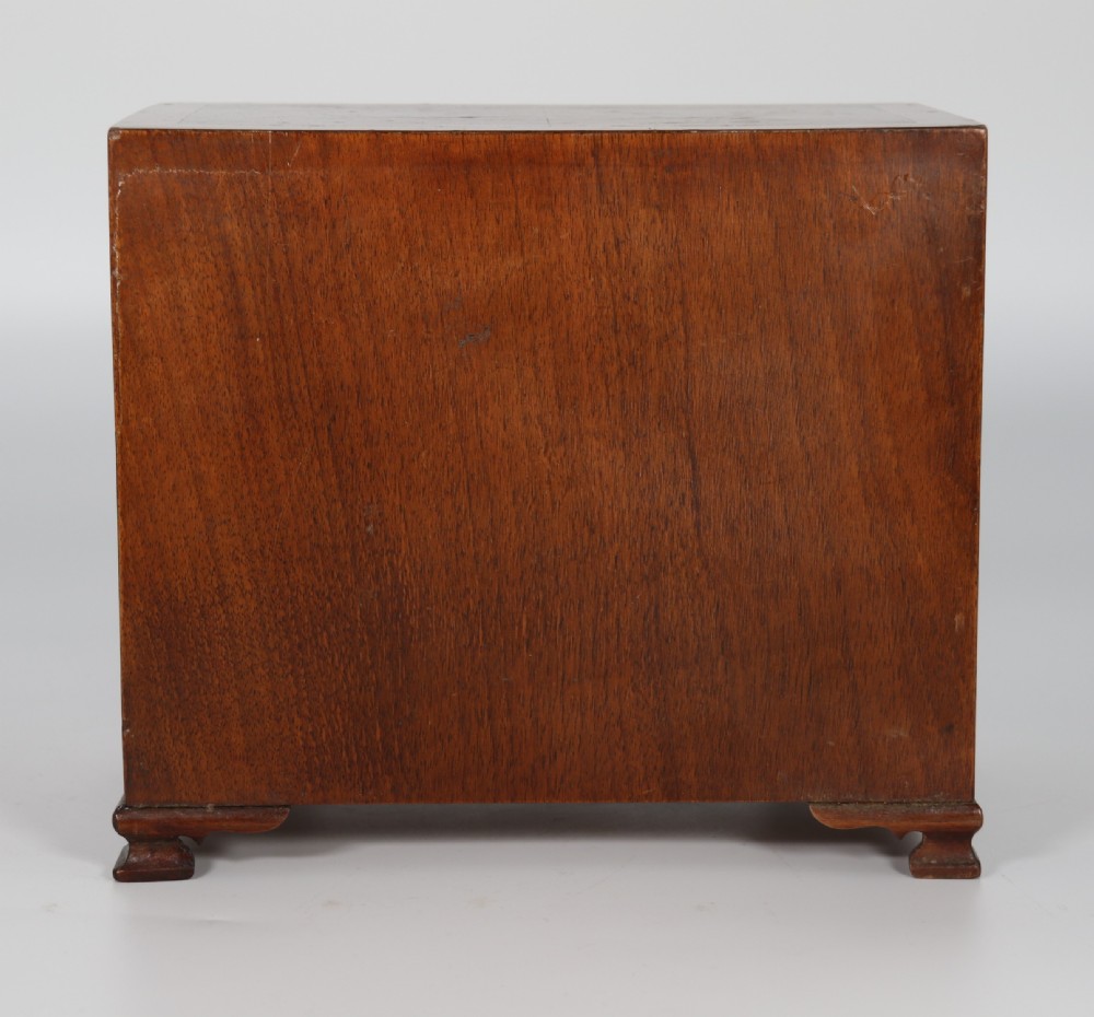 A miniature George II style chest of drawers crafted from figured walnut with brass drop handles, standing 20cm high beside a red apple for scale. View XIX