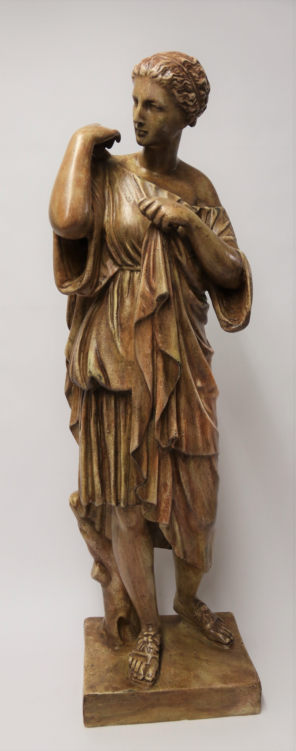 A nineteenth-century Neoclassical sculpture depicting Diana the Huntress draped in classical robes standing on a square base with a warm beige patinated finish.