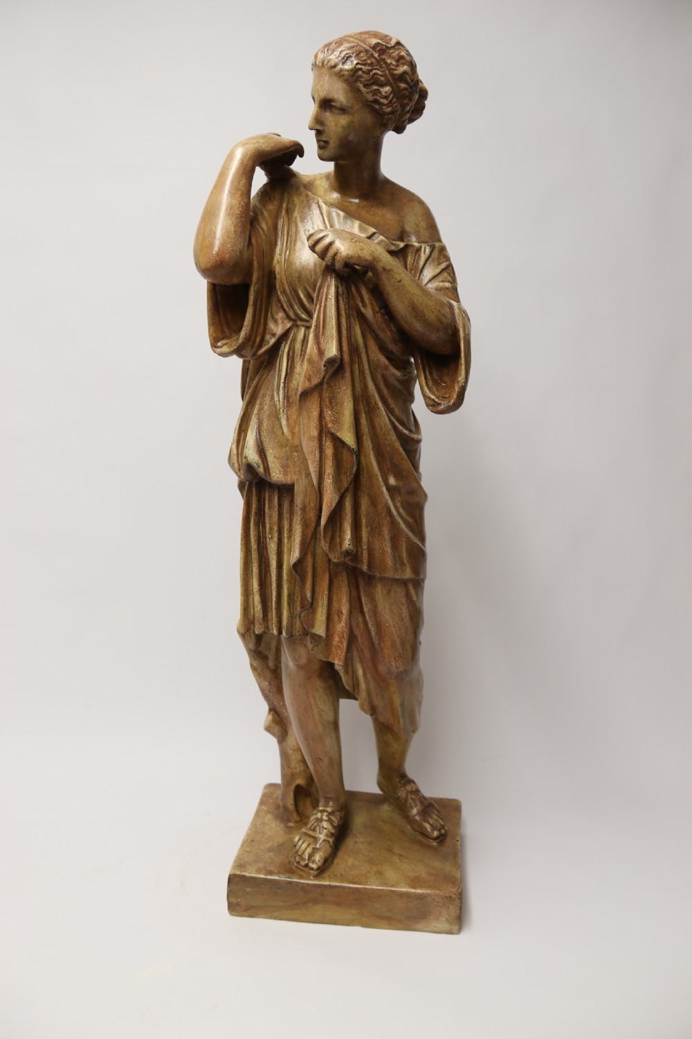 A nineteenth-century Neoclassical sculpture depicting Diana the Huntress draped in classical robes standing on a square base with a warm beige patinated finish. View X