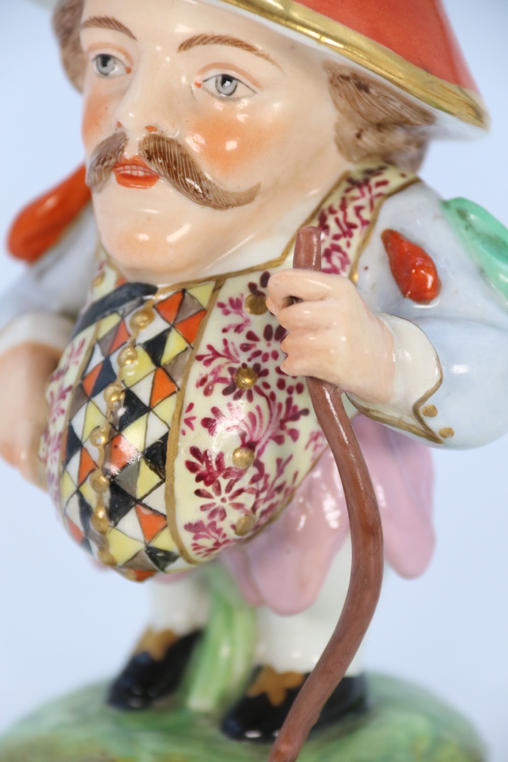 A pair of 19th-century hand-painted Samson porcelain Mansion House dwarf figurines featuring oversized hats and patterned waistcoats. View XXX