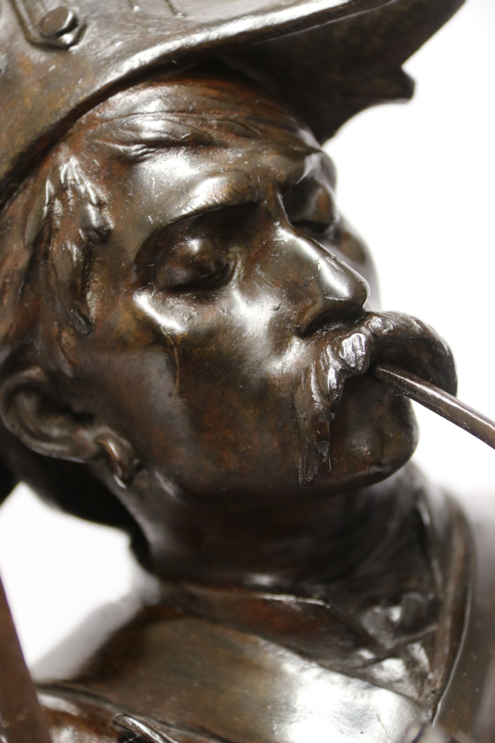 A dark brown patinated bronze sculpture depicting a 1792 French grenadier soldier in full uniform lighting a pipe beside a rifle. View V