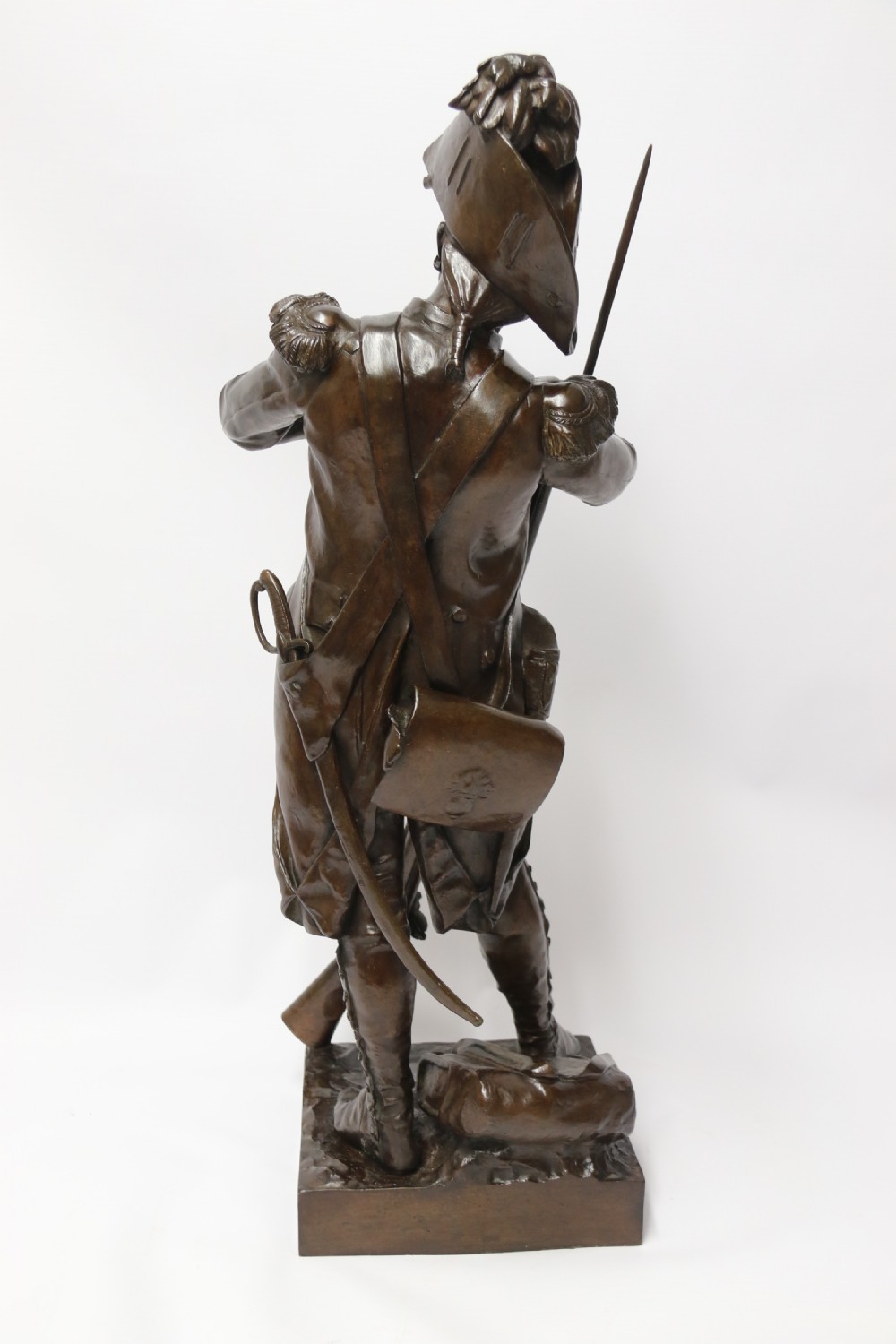 A dark brown patinated bronze sculpture depicting a 1792 French grenadier soldier in full uniform lighting a pipe beside a rifle. View VI