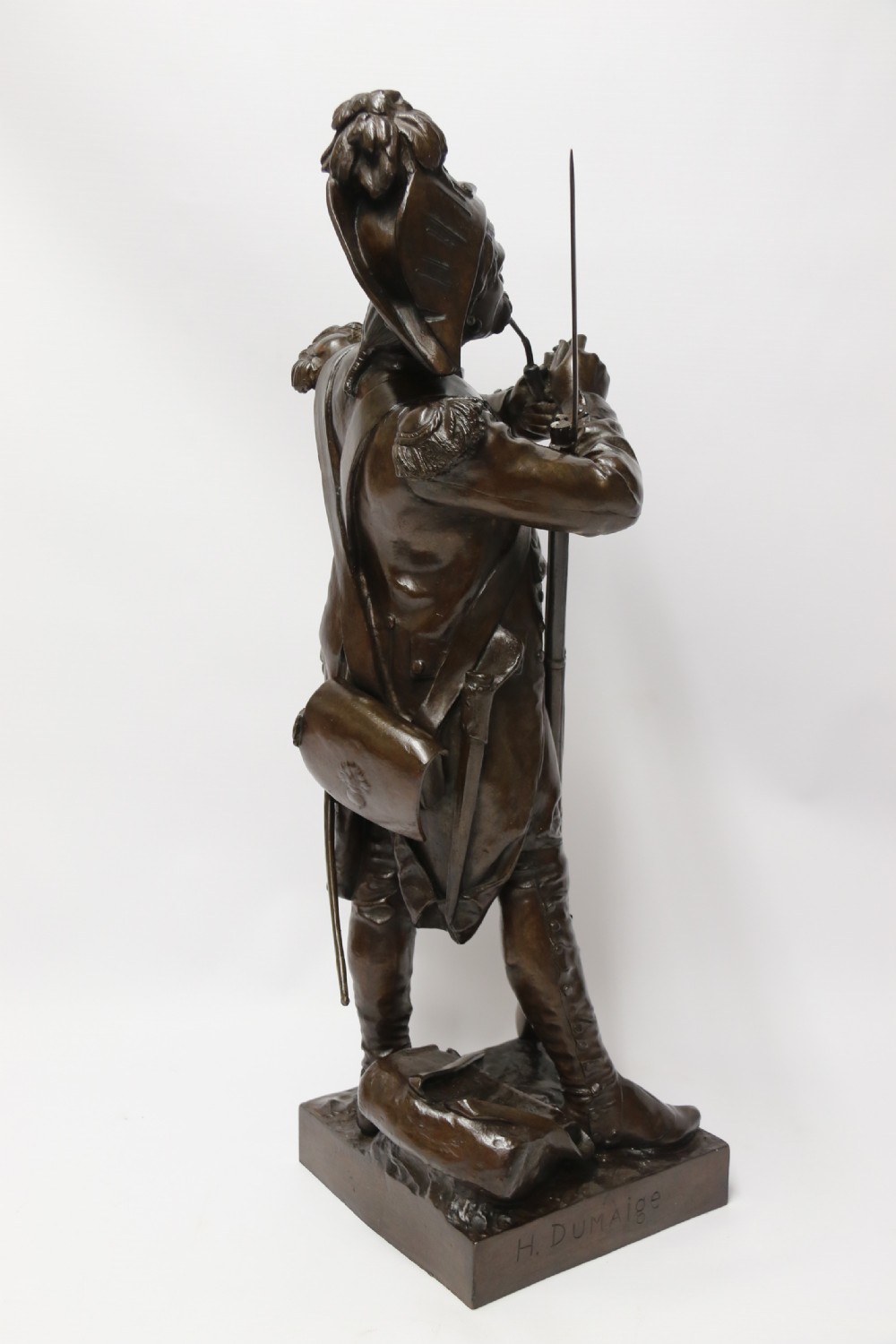 A dark brown patinated bronze sculpture depicting a 1792 French grenadier soldier in full uniform lighting a pipe beside a rifle. View VIII