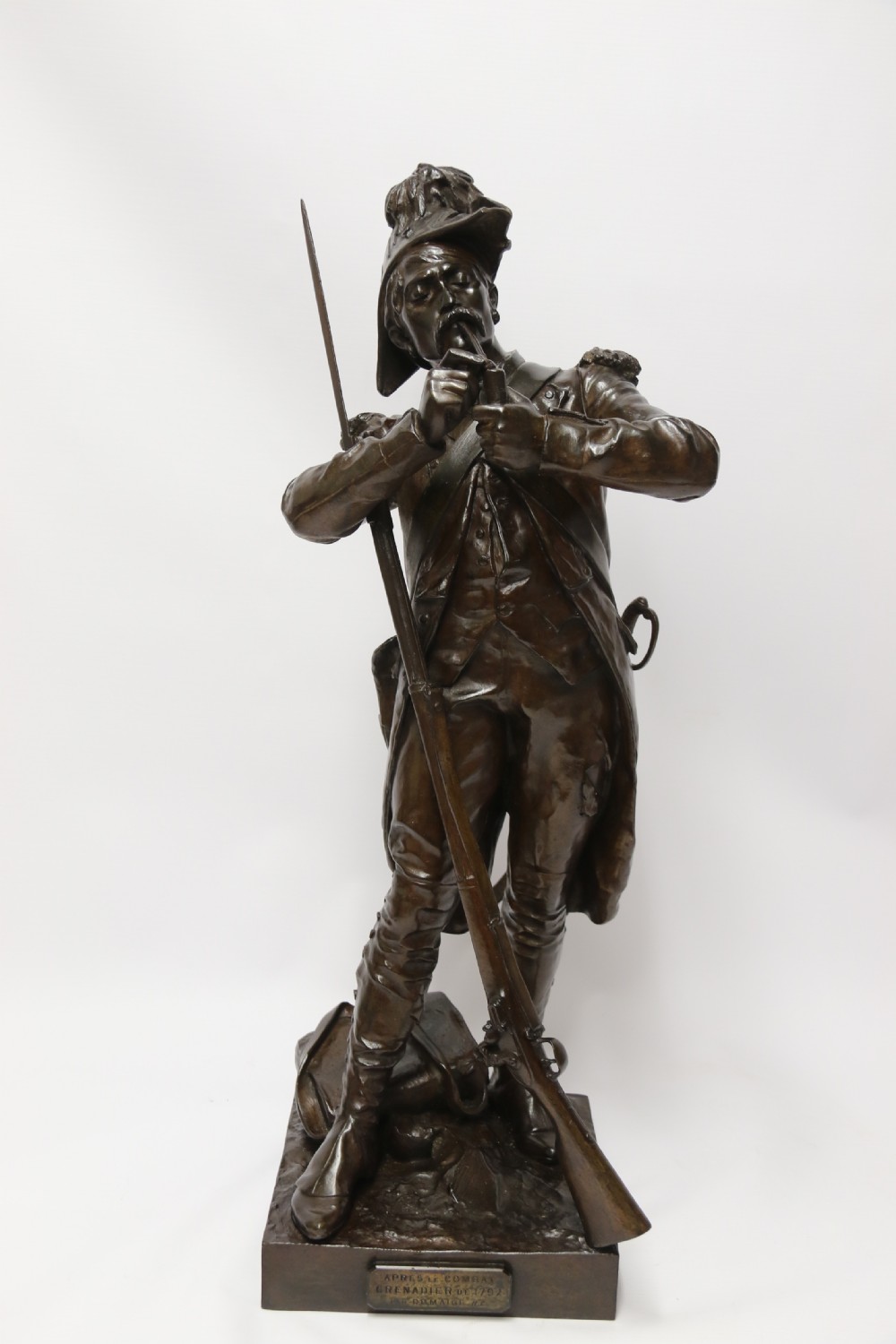 A dark brown patinated bronze sculpture depicting a 1792 French grenadier soldier in full uniform lighting a pipe beside a rifle. View IX
