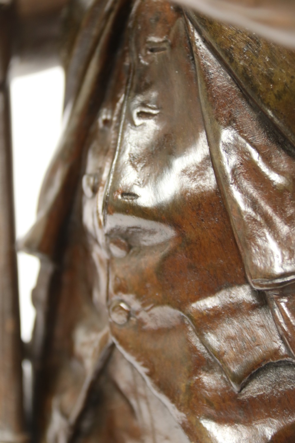 A dark brown patinated bronze sculpture depicting a 1792 French grenadier soldier in full uniform lighting a pipe beside a rifle. View XI