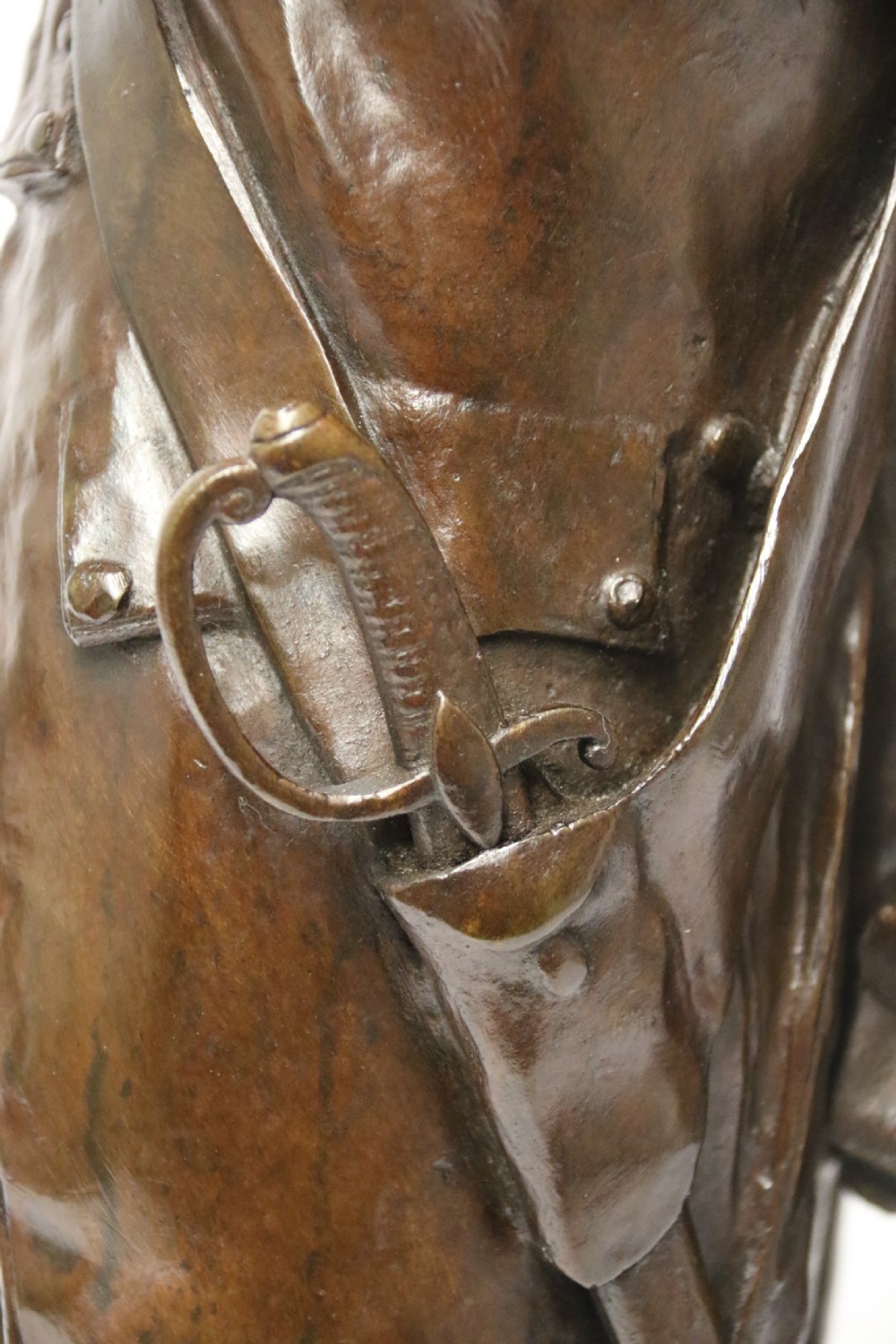 A dark brown patinated bronze sculpture depicting a 1792 French grenadier soldier in full uniform lighting a pipe beside a rifle. View XIII
