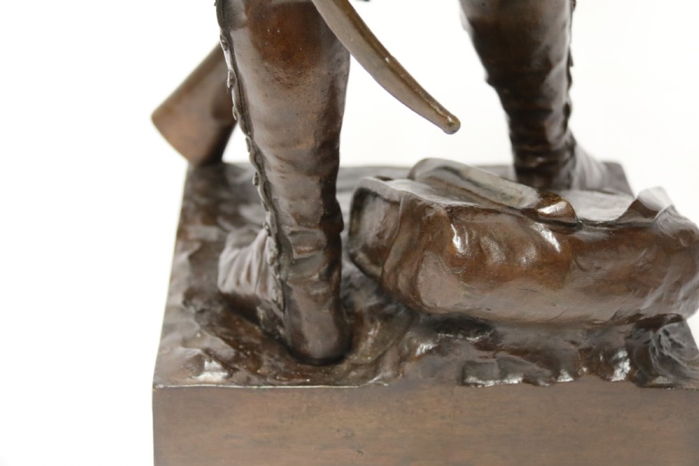 A dark brown patinated bronze sculpture depicting a 1792 French grenadier soldier in full uniform lighting a pipe beside a rifle. View XVII