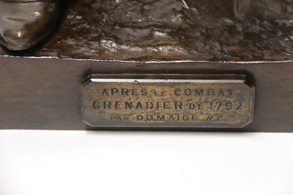 A dark brown patinated bronze sculpture depicting a 1792 French grenadier soldier in full uniform lighting a pipe beside a rifle. View XIX