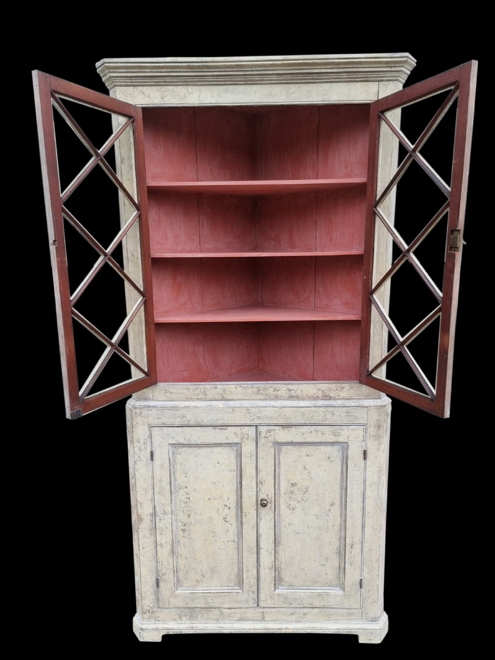 A two-part Georgian painted corner cupboard featuring astragal glazed upper doors revealing a red interior above a double-panelled lower cabinet. View II