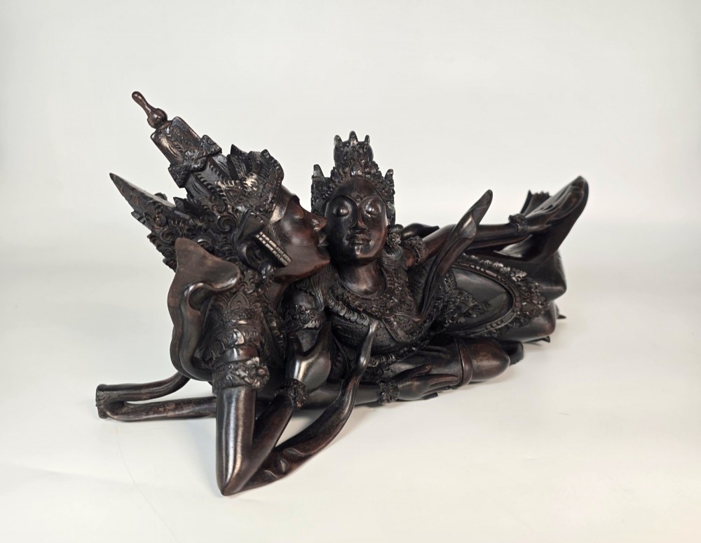 A dark hardwood Balinese carving depicting the reclining figures of Rama and Sita with detailed ornate headdresses and traditional attire. View II