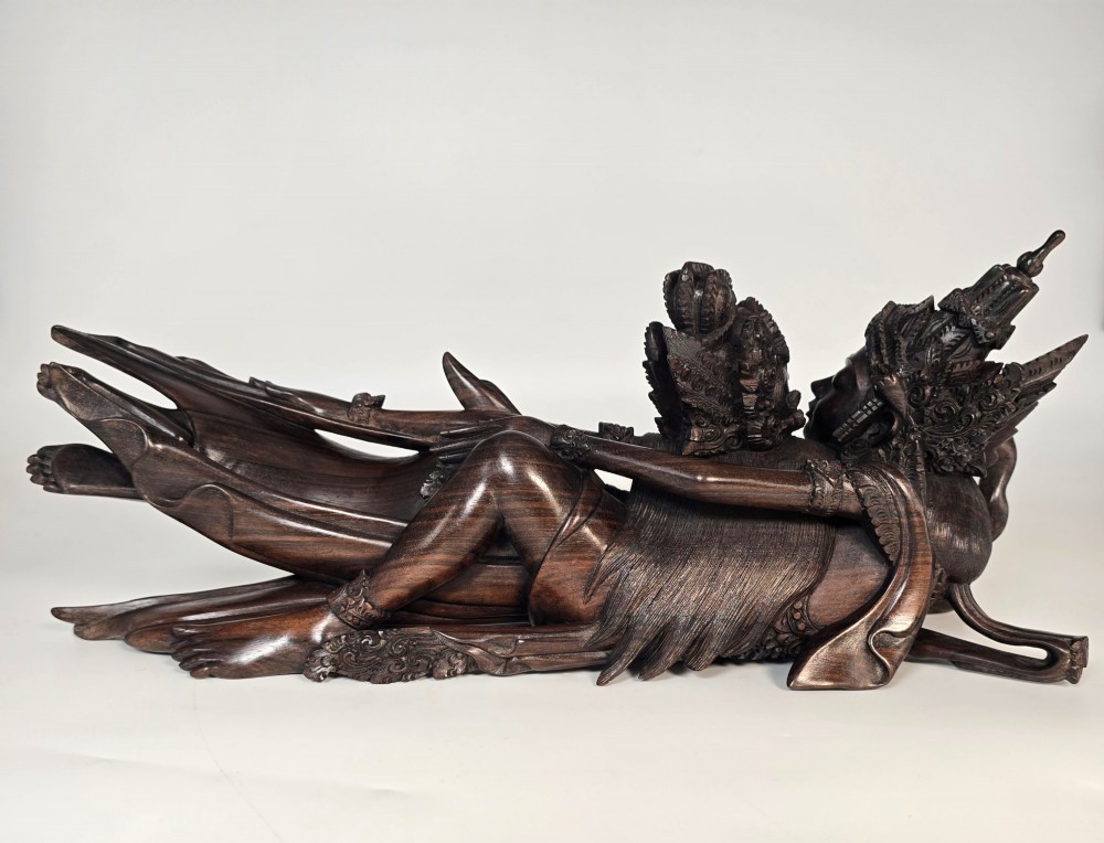 A dark hardwood Balinese carving depicting the reclining figures of Rama and Sita with detailed ornate headdresses and traditional attire. View V