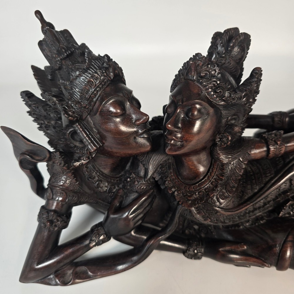 A dark hardwood Balinese carving depicting the reclining figures of Rama and Sita with detailed ornate headdresses and traditional attire. View VI
