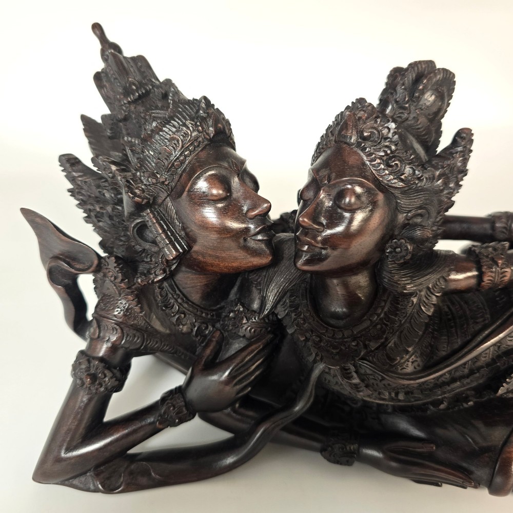 A dark hardwood Balinese carving depicting the reclining figures of Rama and Sita with detailed ornate headdresses and traditional attire. View XII