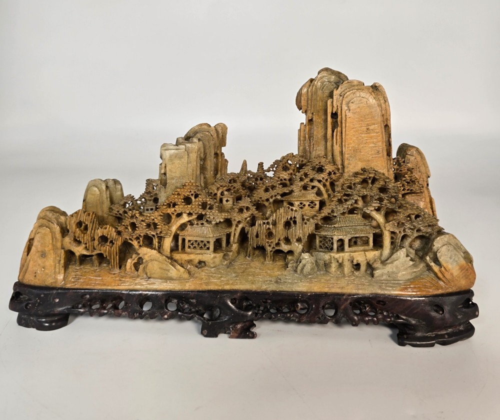 A carved Chinese soapstone continuous landscape featuring mountain peaks, pine trees, and pavilions set upon a fitted dark carved hardwood stand. View II