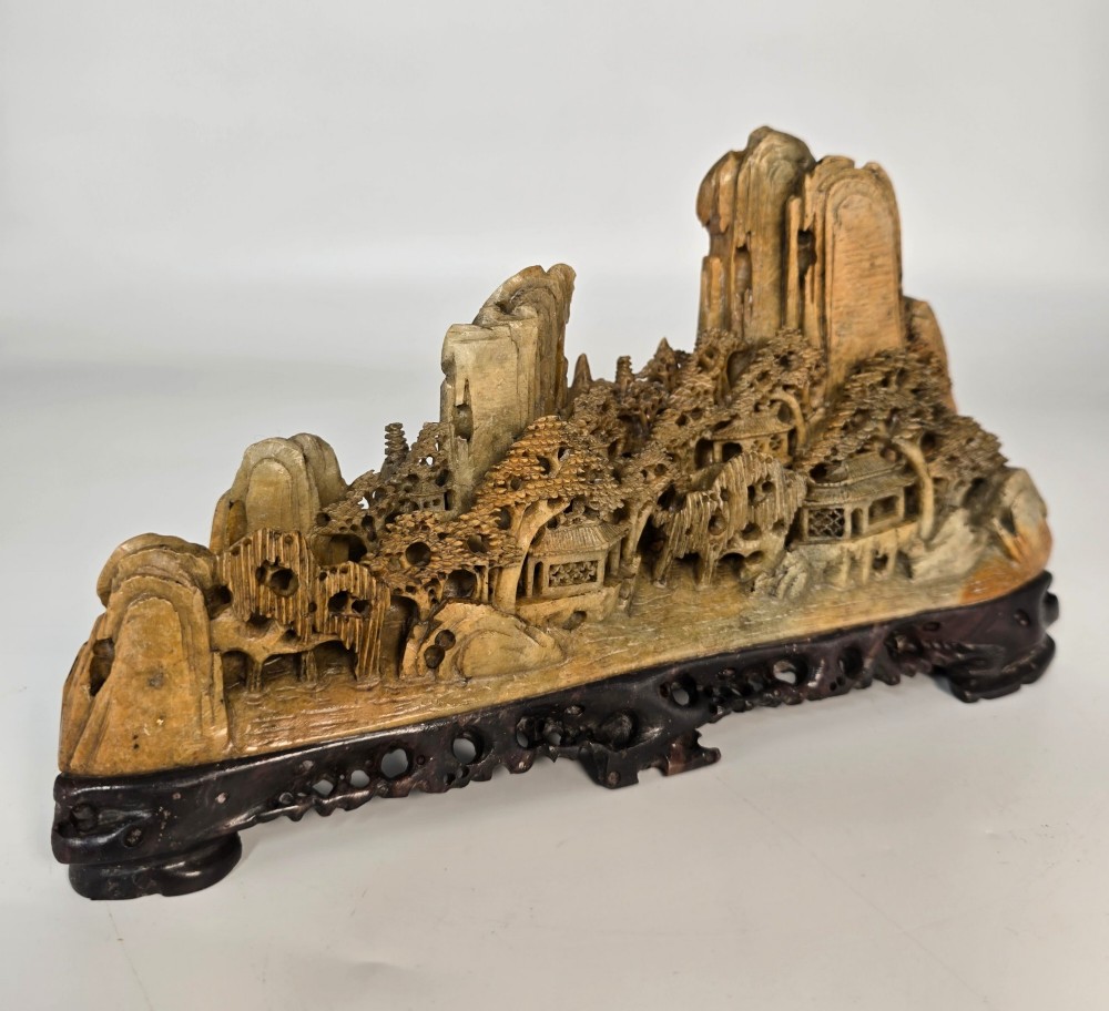 A carved Chinese soapstone continuous landscape featuring mountain peaks, pine trees, and pavilions set upon a fitted dark carved hardwood stand. View III