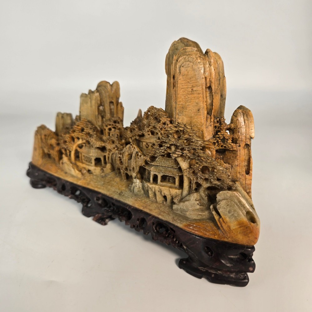 A carved Chinese soapstone continuous landscape featuring mountain peaks, pine trees, and pavilions set upon a fitted dark carved hardwood stand. View IV