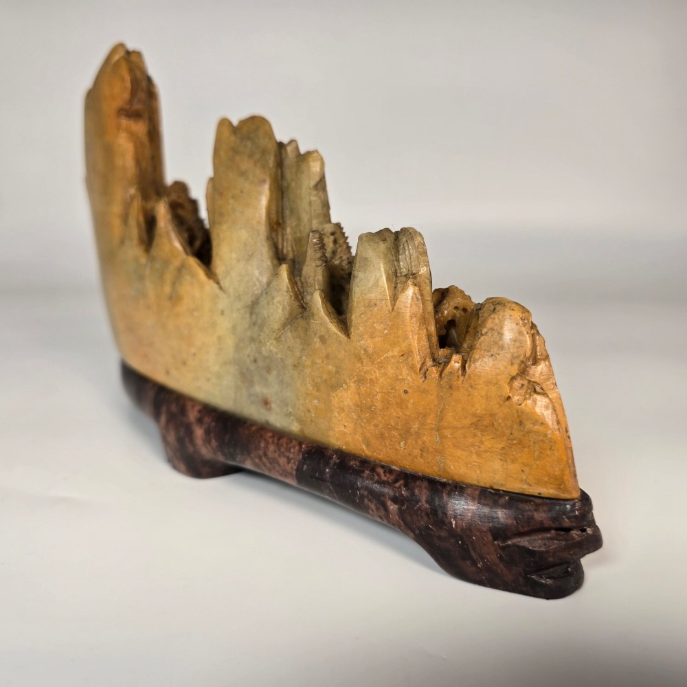 A carved Chinese soapstone continuous landscape featuring mountain peaks, pine trees, and pavilions set upon a fitted dark carved hardwood stand. View VII