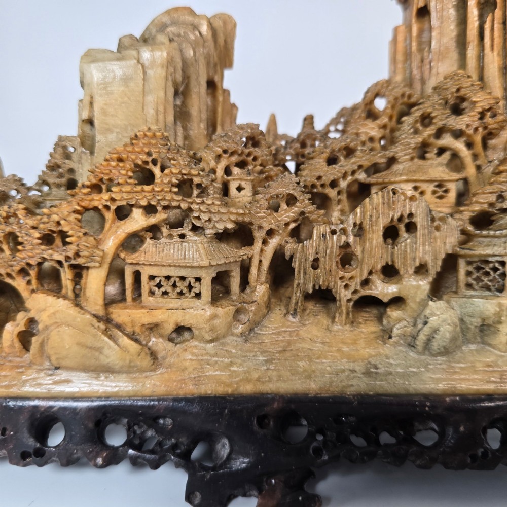 A carved Chinese soapstone continuous landscape featuring mountain peaks, pine trees, and pavilions set upon a fitted dark carved hardwood stand. View IX