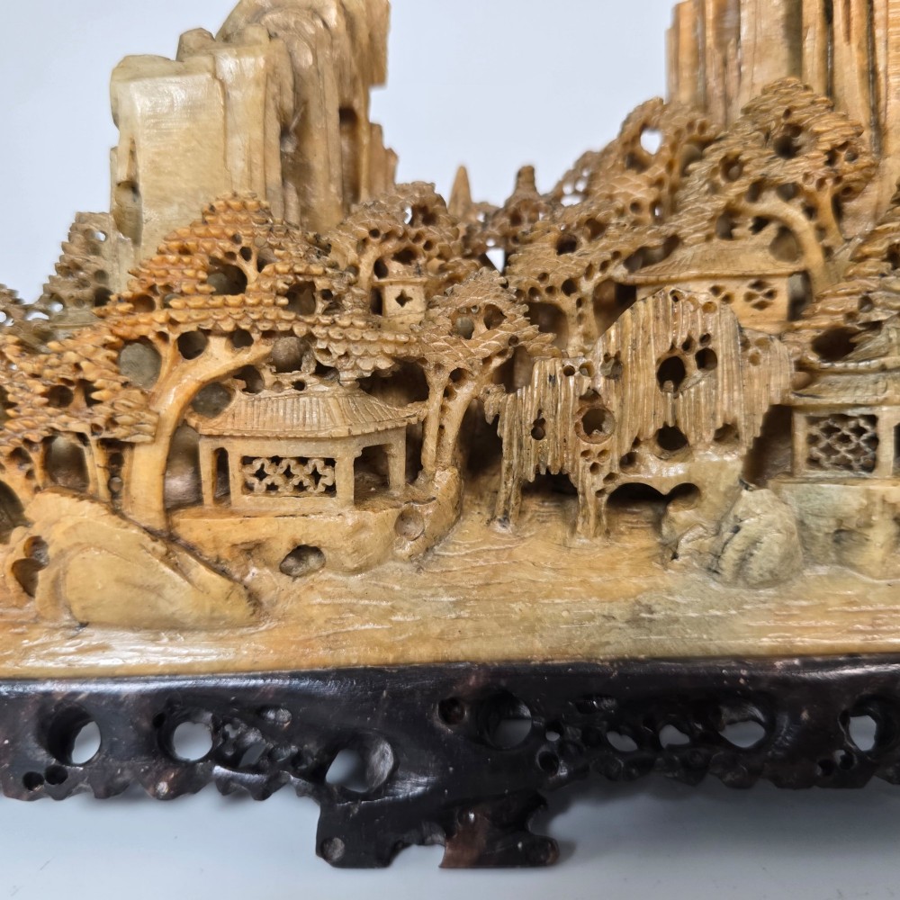 A carved Chinese soapstone continuous landscape featuring mountain peaks, pine trees, and pavilions set upon a fitted dark carved hardwood stand. View X