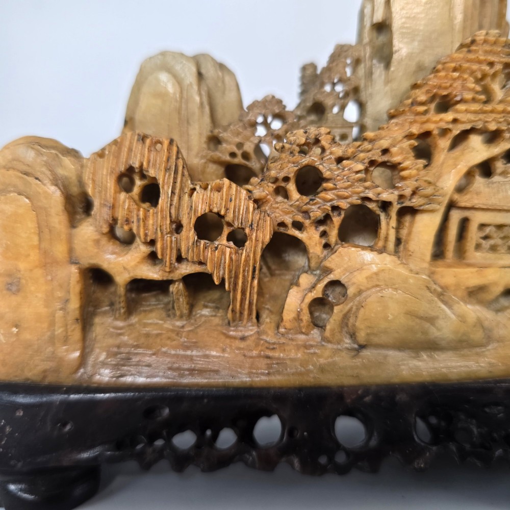 A carved Chinese soapstone continuous landscape featuring mountain peaks, pine trees, and pavilions set upon a fitted dark carved hardwood stand. View XI