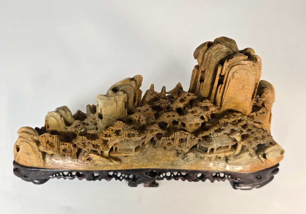 A carved Chinese soapstone continuous landscape featuring mountain peaks, pine trees, and pavilions set upon a fitted dark carved hardwood stand. View XV