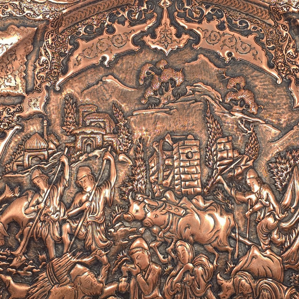 A circular Persian copper charger featuring detailed central repousse relief surrounded by intricate arabesque and paisley borders. View V